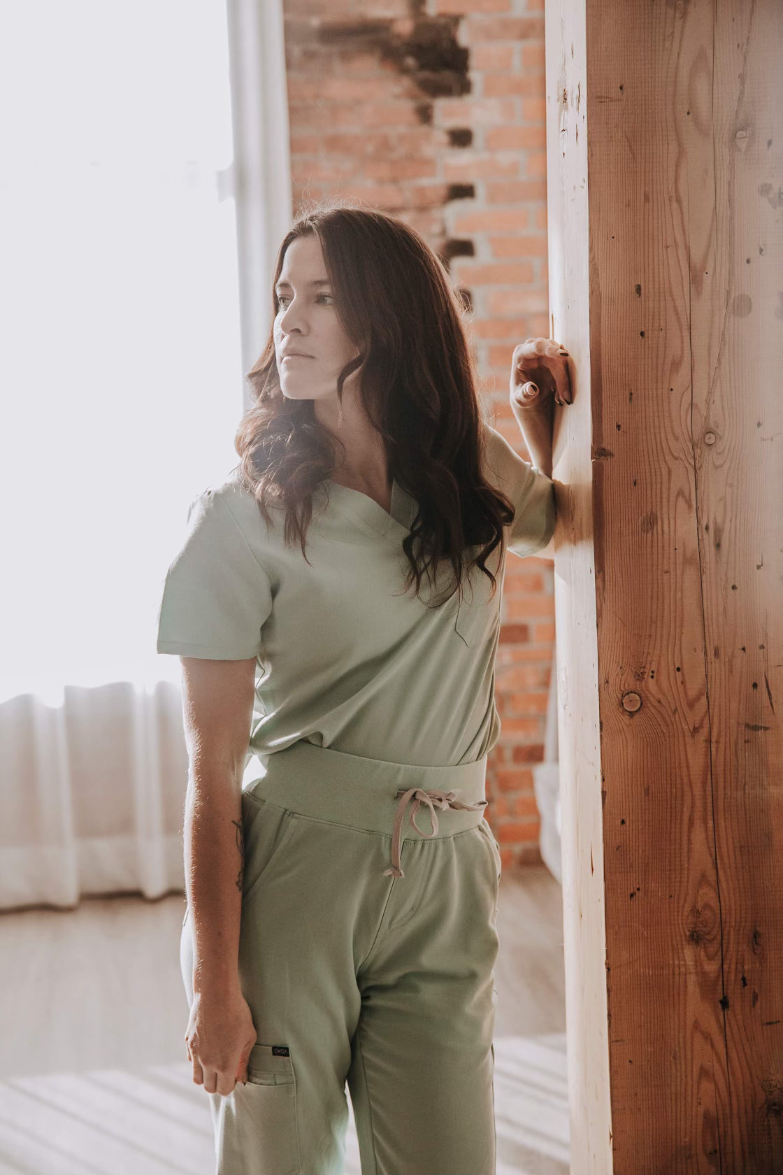 Women in a sage KOA scrub set - V-neck top and high-rise joggers with contrast drawstring