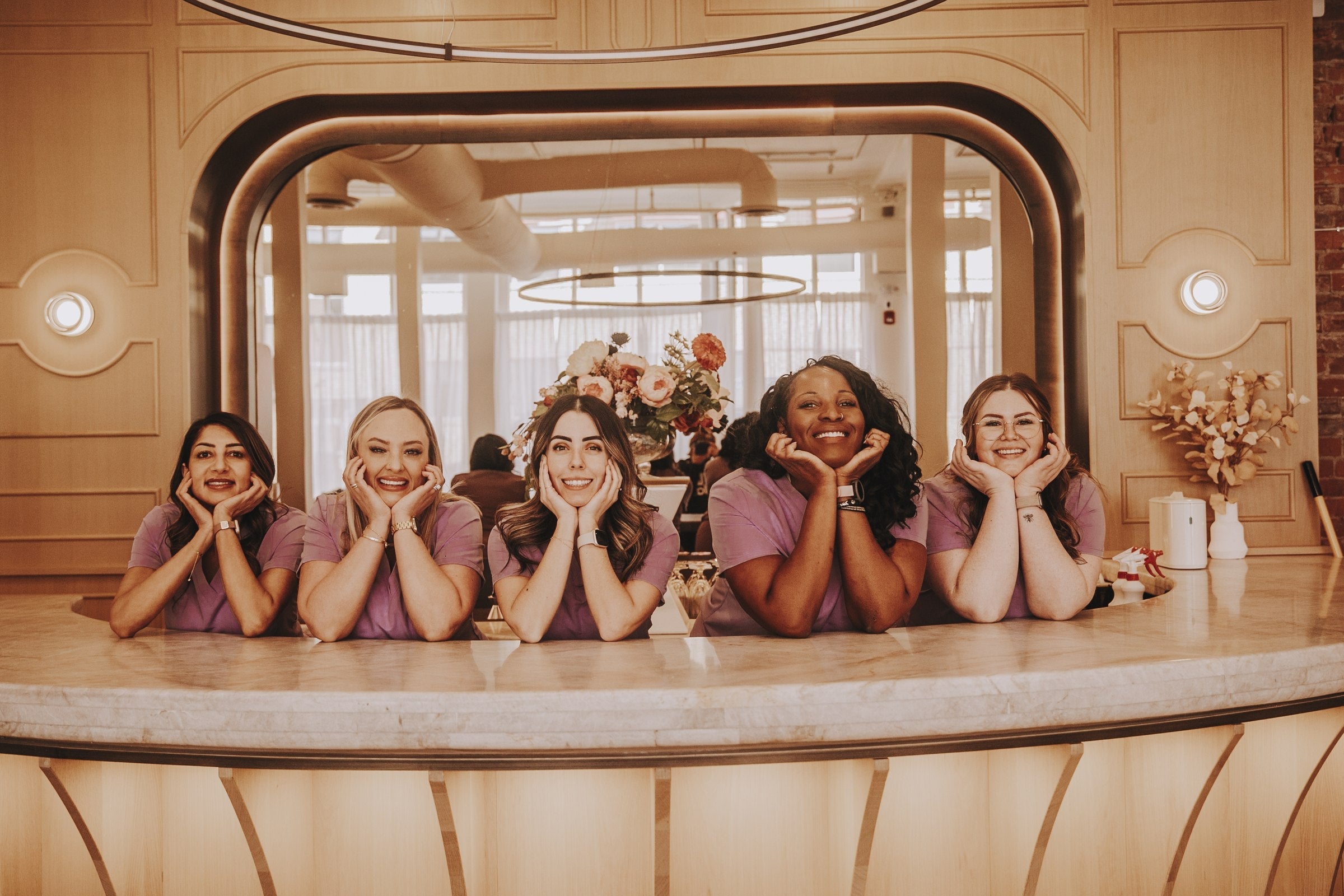 Five clinic staff in mauve KOA scrub tops leaning on a reception desk