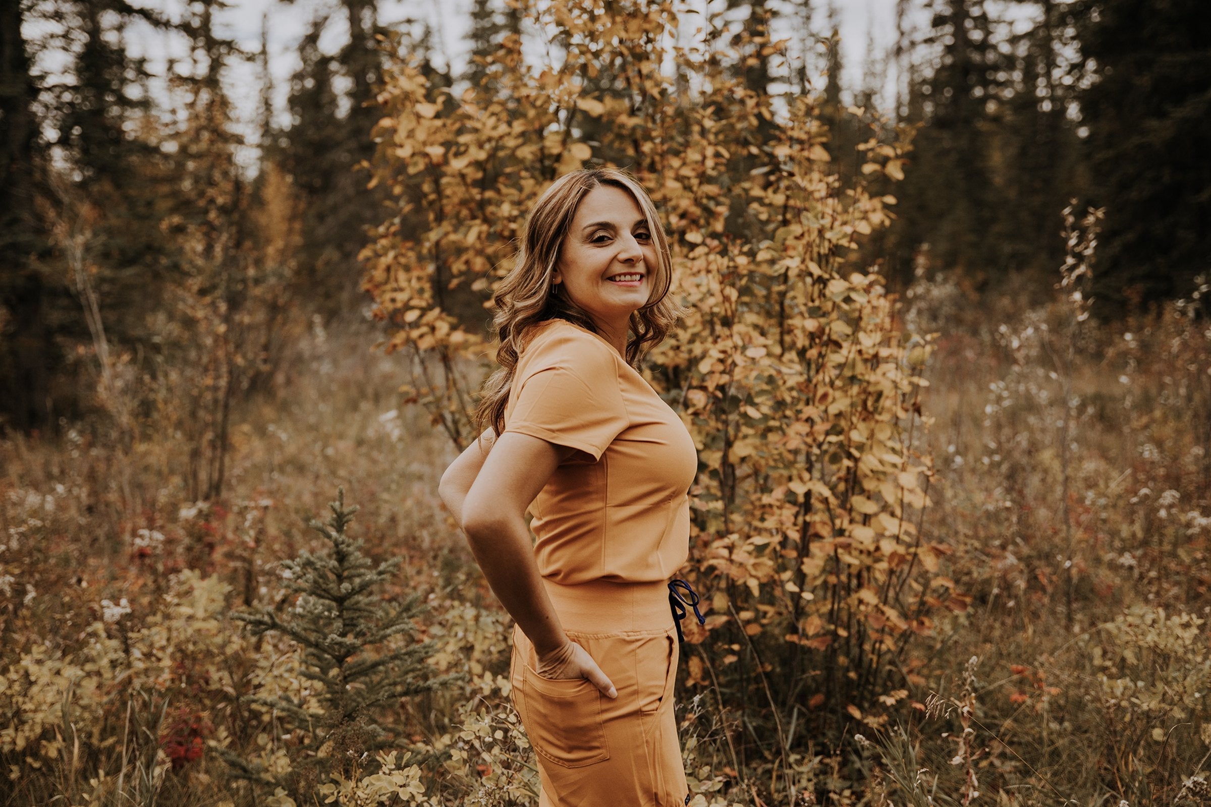 Healthcare worker in a turmeric KOA scrub set standing in autumn brush