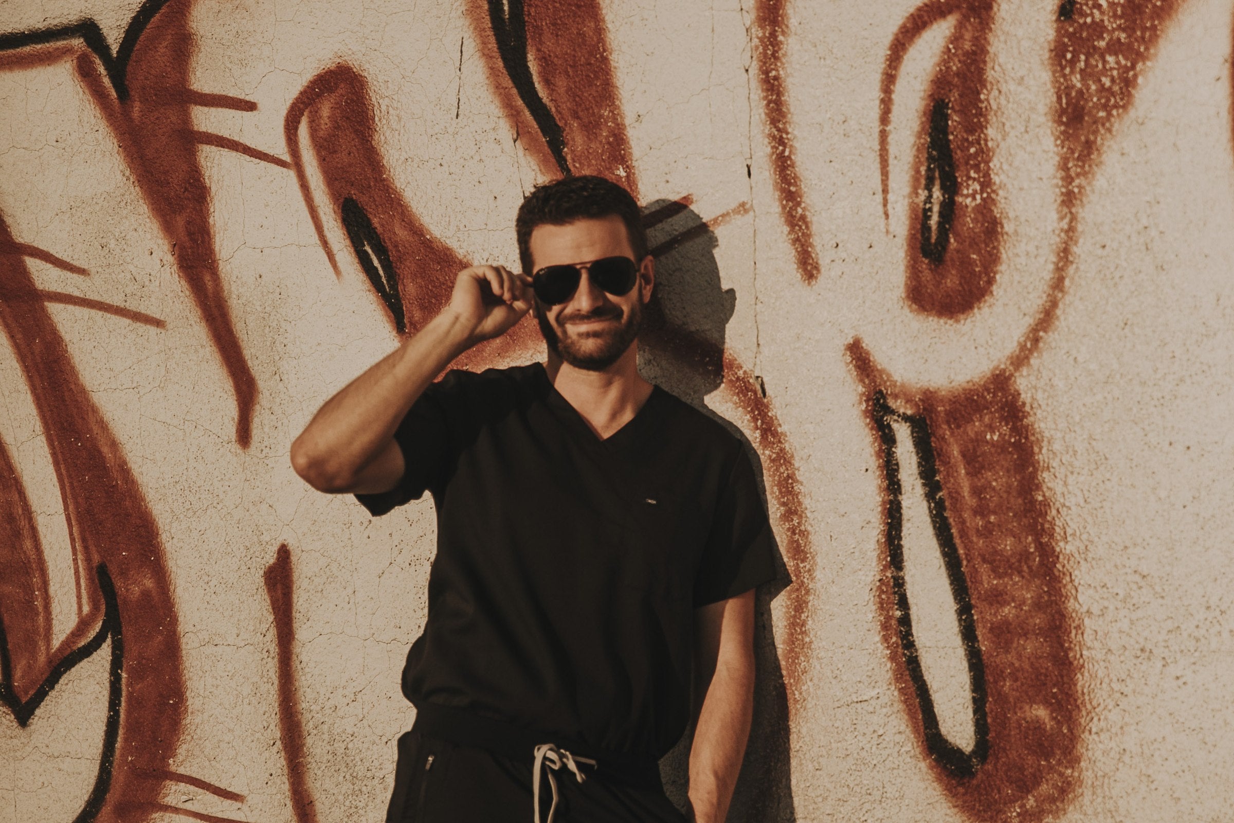 Healthcare worker in a black KOA scrub set standing against a graffiti wall