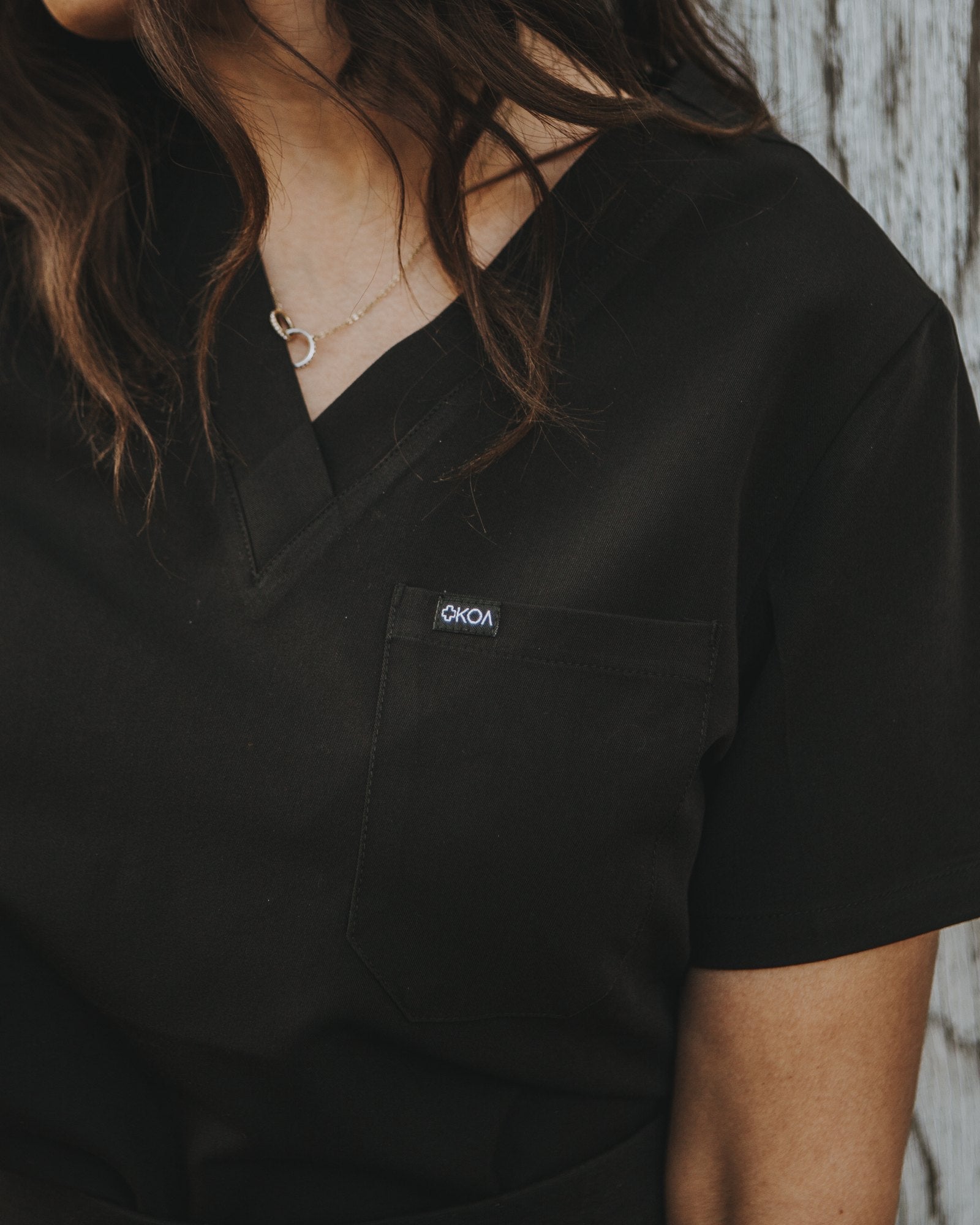 Chest pocket and KOA label detail on the black Women's One Pocket Scrub Top