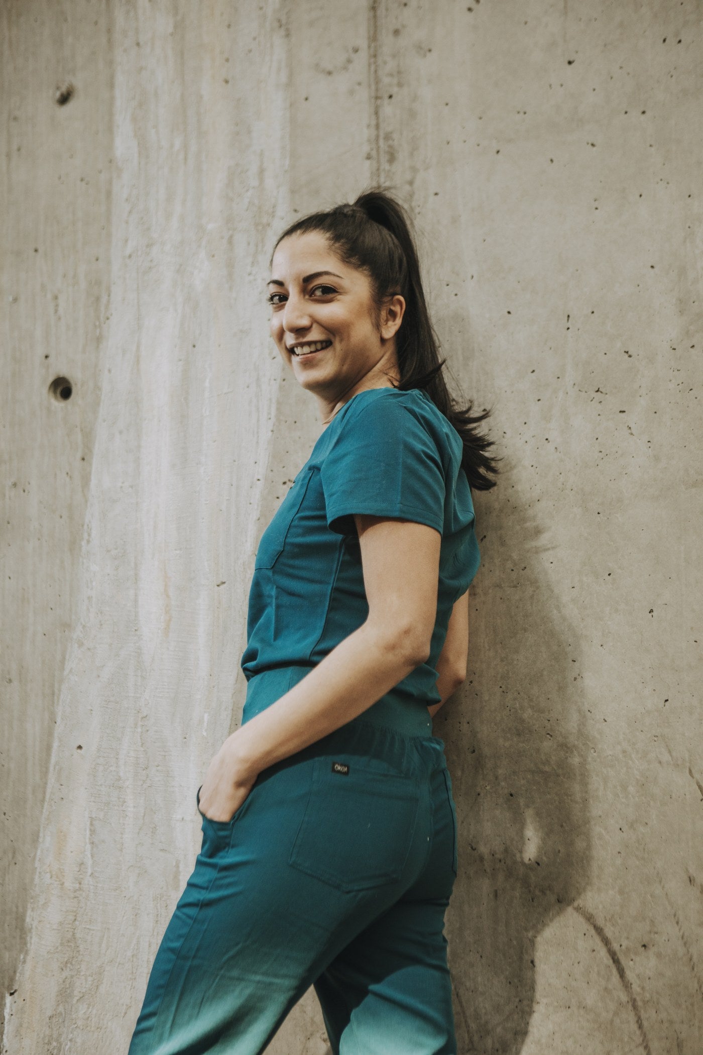 Healthcare worker in a matched teal KOA scrub set against a concrete wall